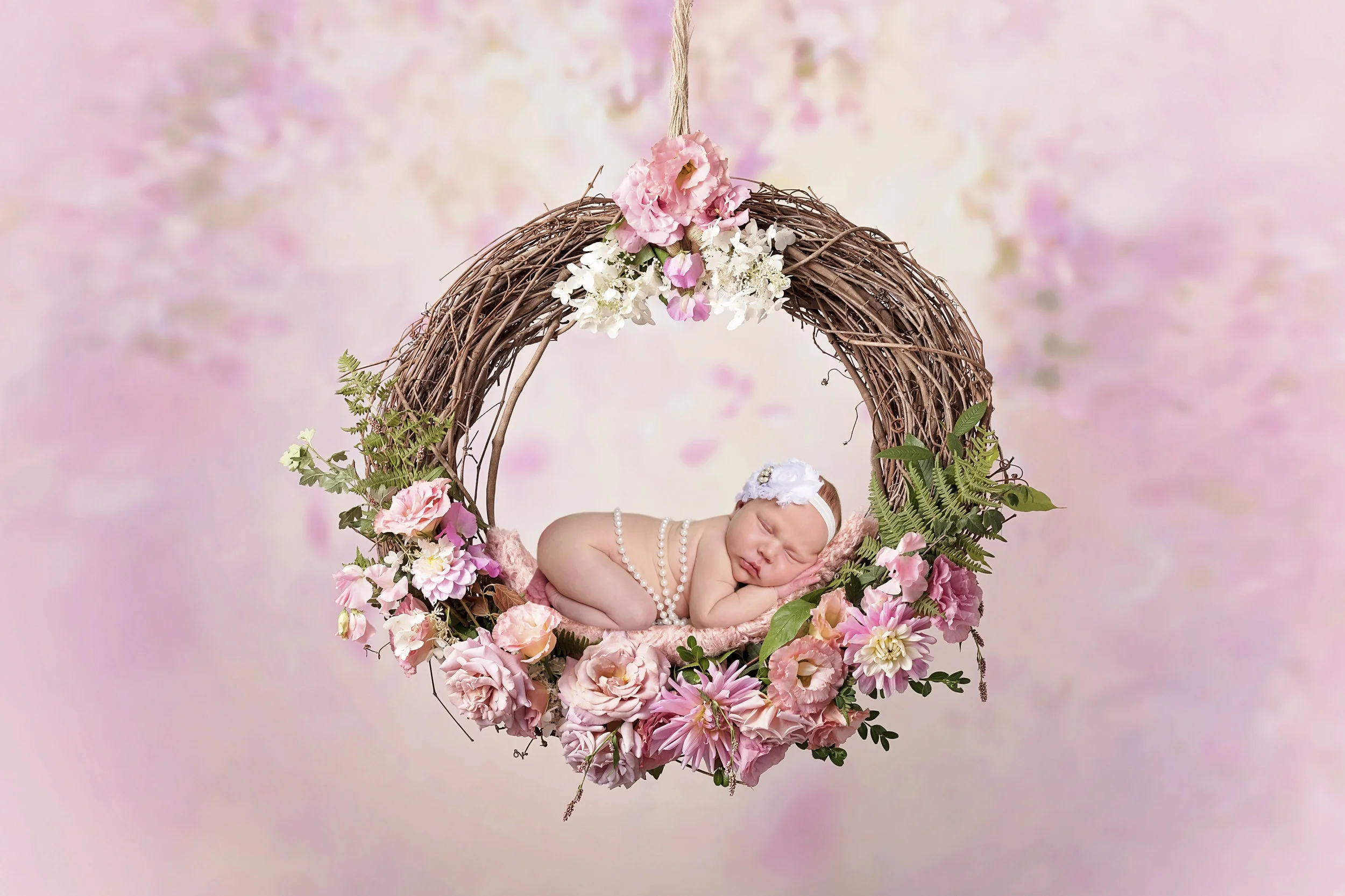 Newborn baby sleeping in a pink floral wreath during a professional newborn photography session in Navarre, Florida.