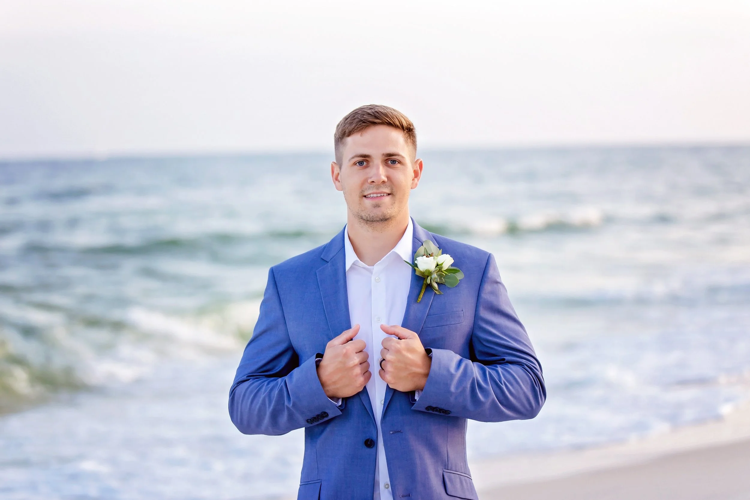 Groom standing on the white sands of Orange beach in Alabama holding his blue blazer for a picture