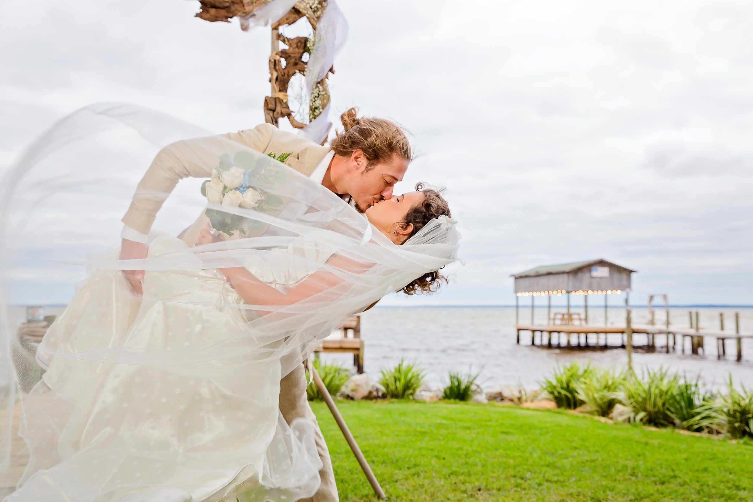 Bride and groom on their wedding day kissing under the arbor at the Bay Front Lodge and Log Cabin In Gulf Breeze Florida Pictures were taken by a St. Augustine Wedding photographer