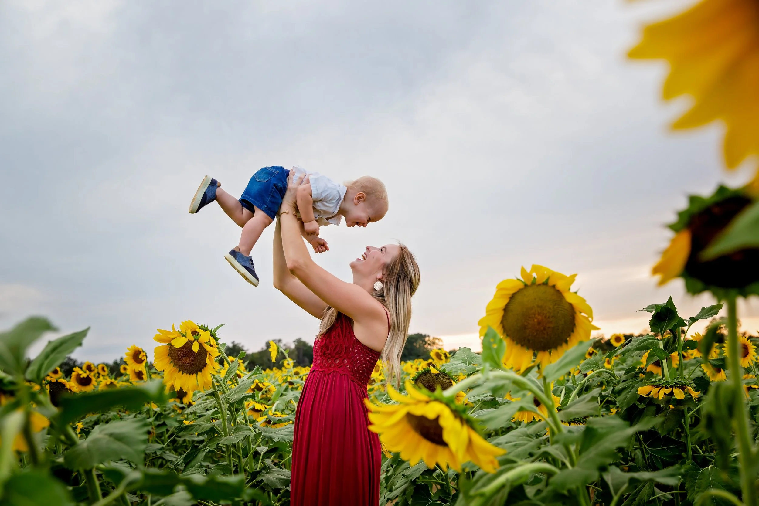 A family photo of a mom holding her son in the middle of a sunflower field in Jacksonville Florida
