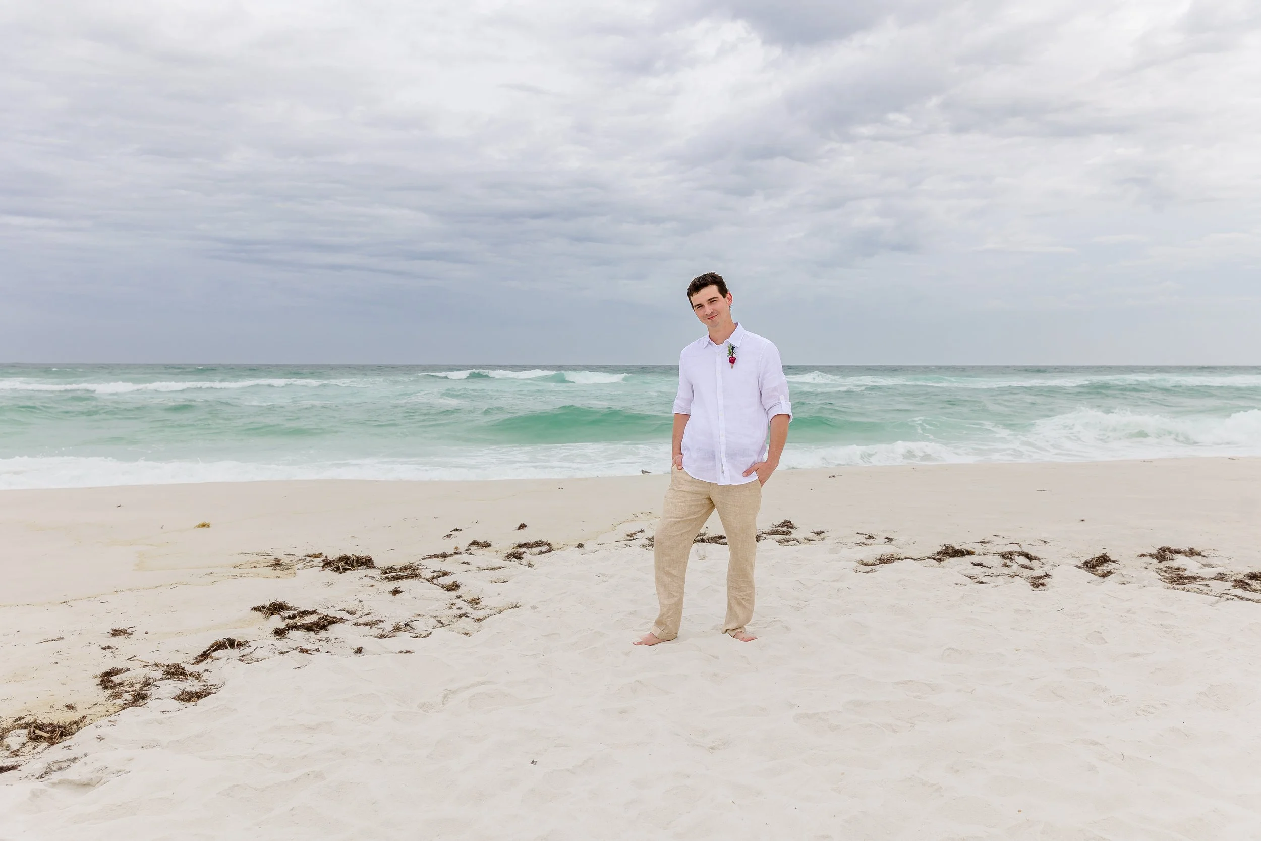 handsome groom posing for portraits standing on white sandy Navarre beach picture by Jacksonville beach and St. Augustine wedding photographer