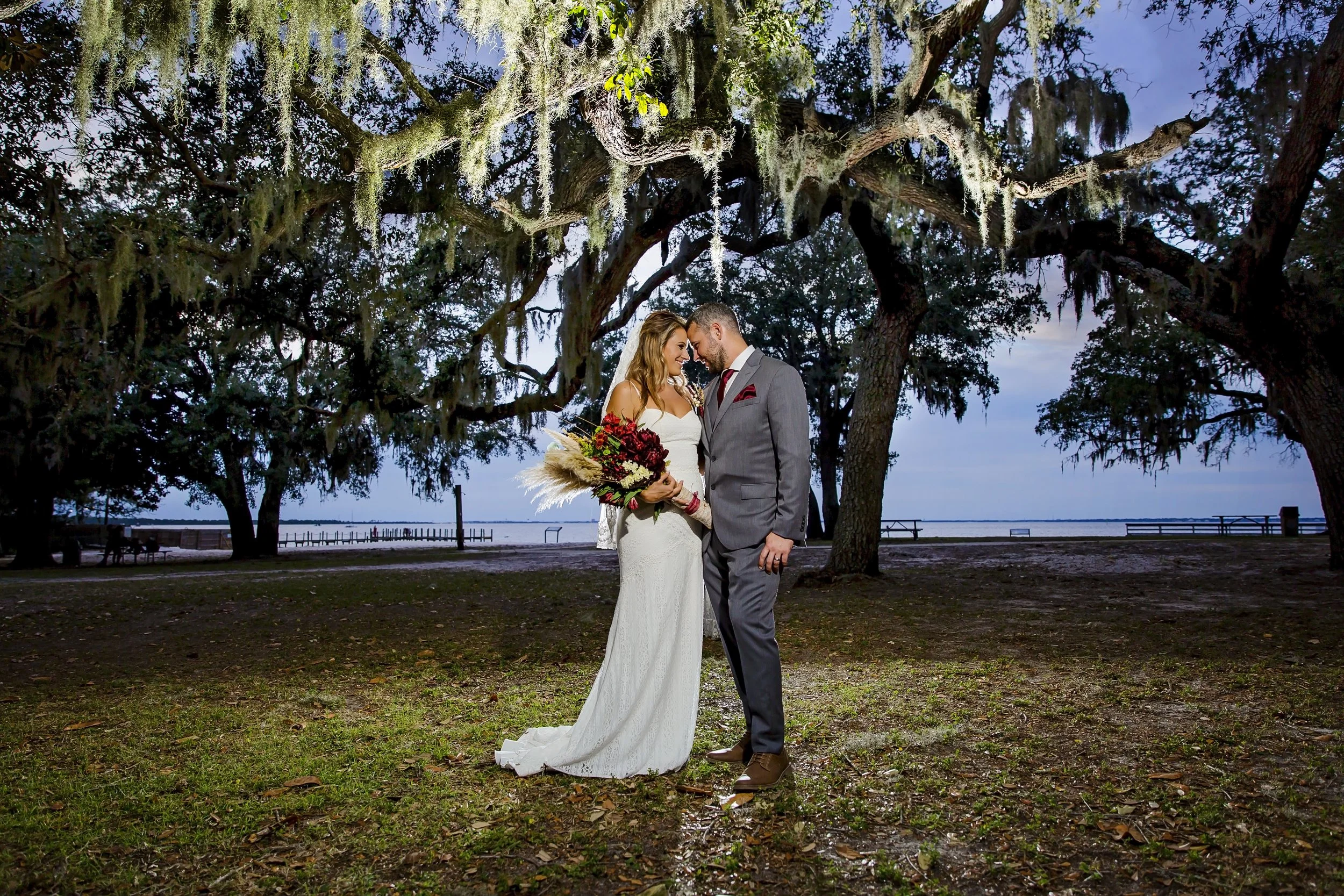 Bride and Groom standing next to each other under a tree covered in Spanish with their foreheads touching taken by a Jacksonville St. Augustine beach photographer