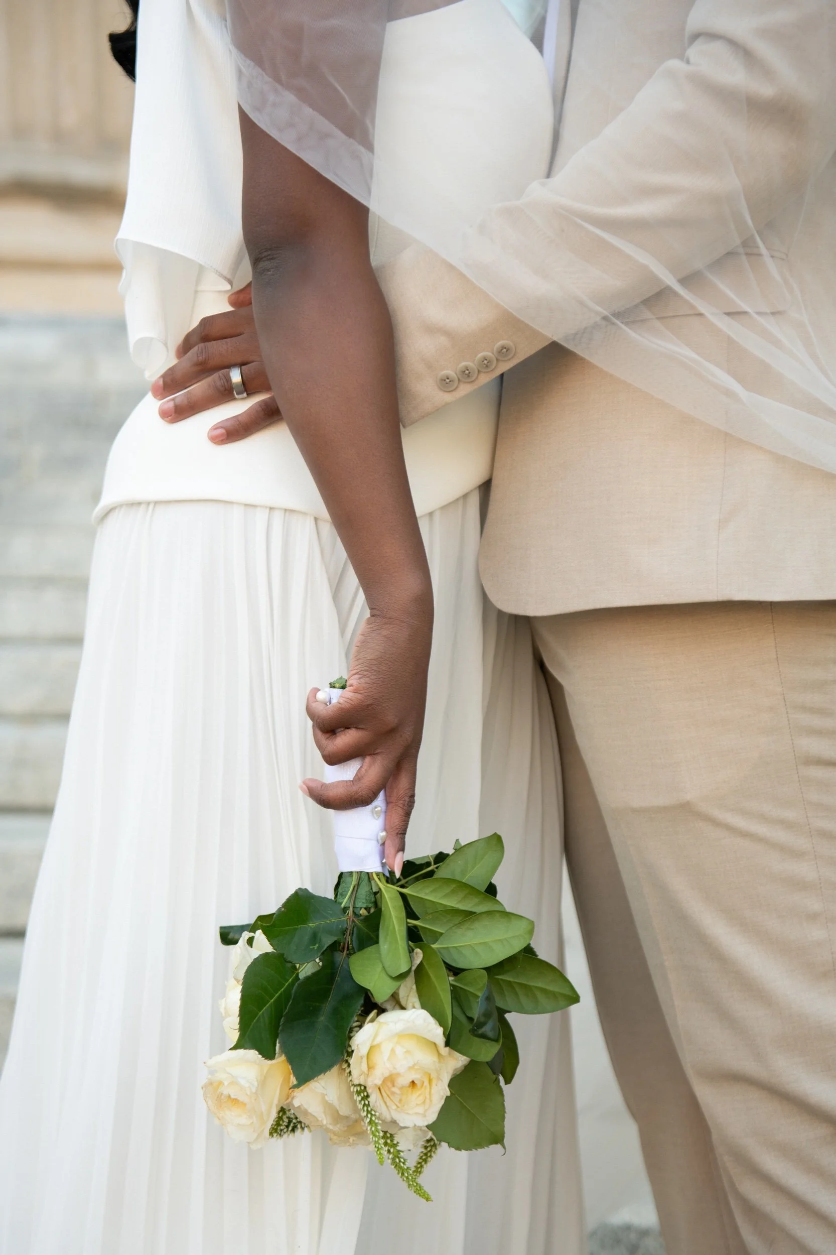 Close-up of a bride and groom holding a bouquet of white roses and green leaves during a wedding ceremony.