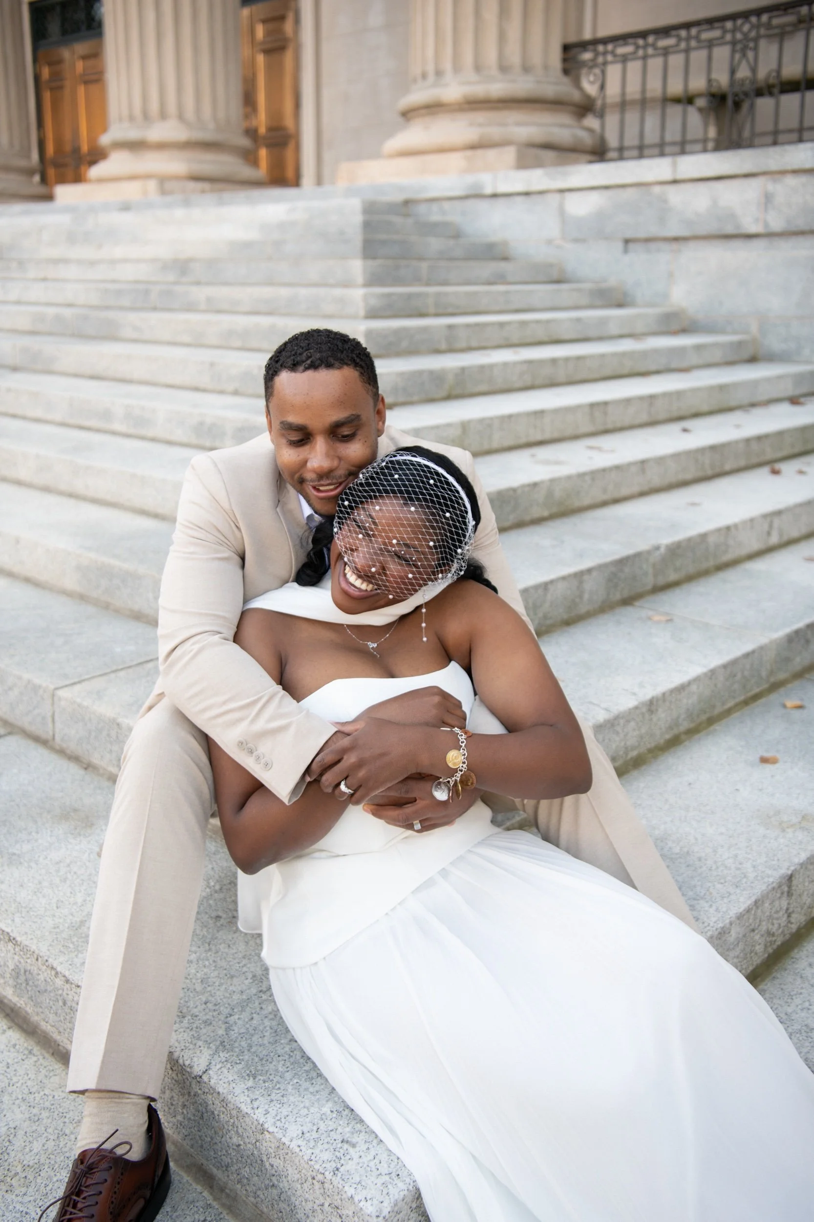 A joyful bride and groom sharing a hug on the steps of a building with large columns.