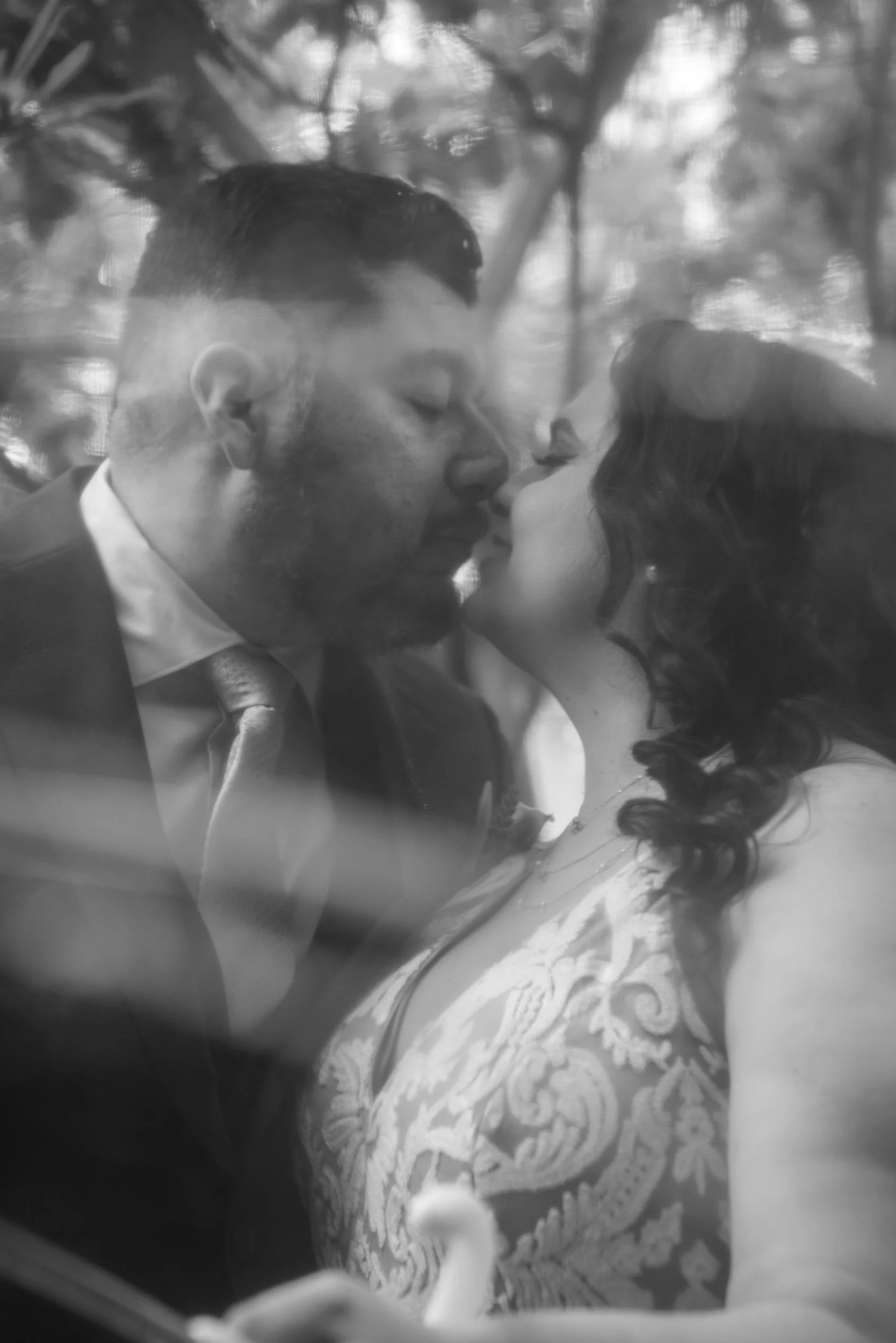 A black and white photo of a couple about to kiss, with the man in a suit and the woman in a dress with floral embroidery.