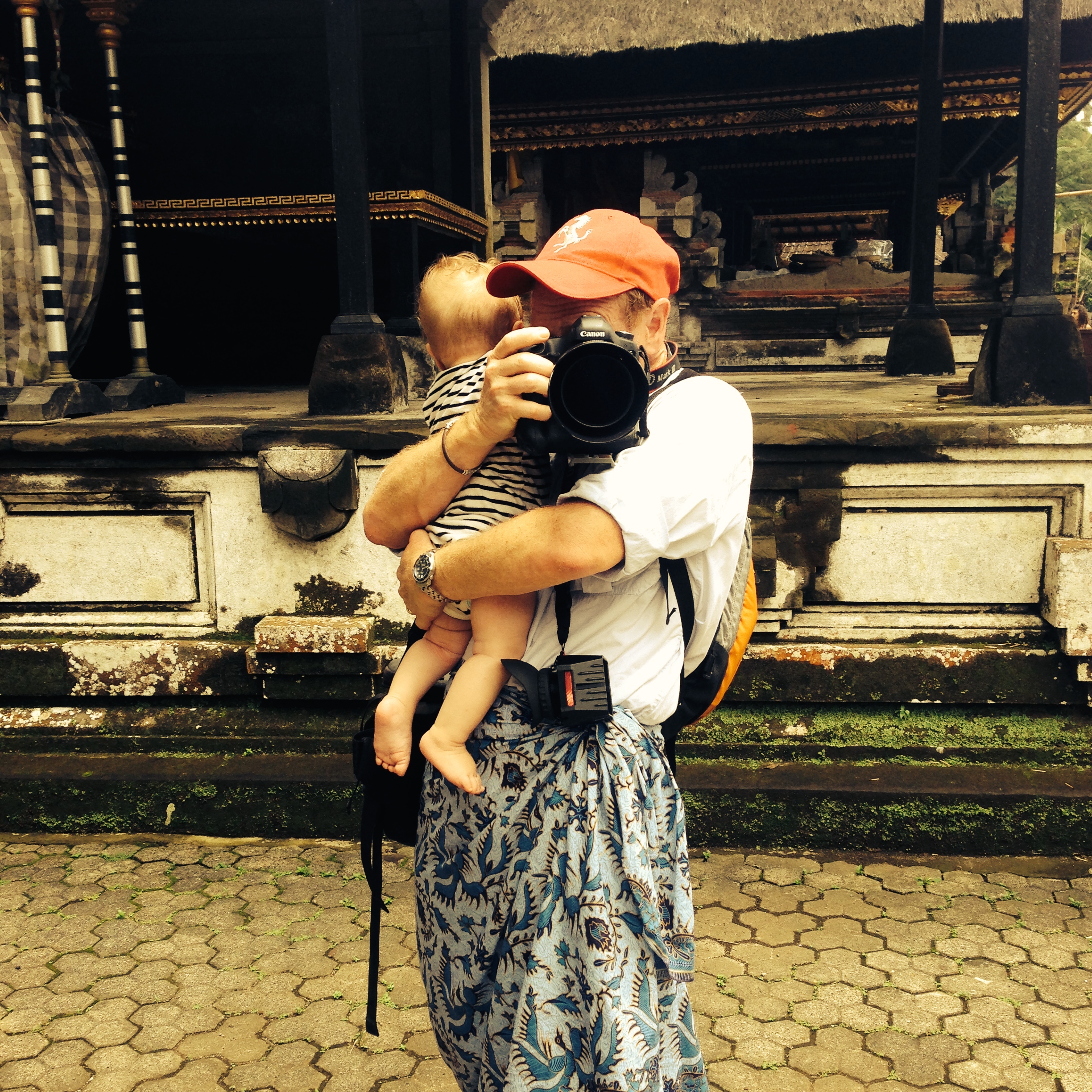 Multi-tasking Mr. Mom holding his 6 month old son at Tampaksiring temple in Bali, Indonesia
