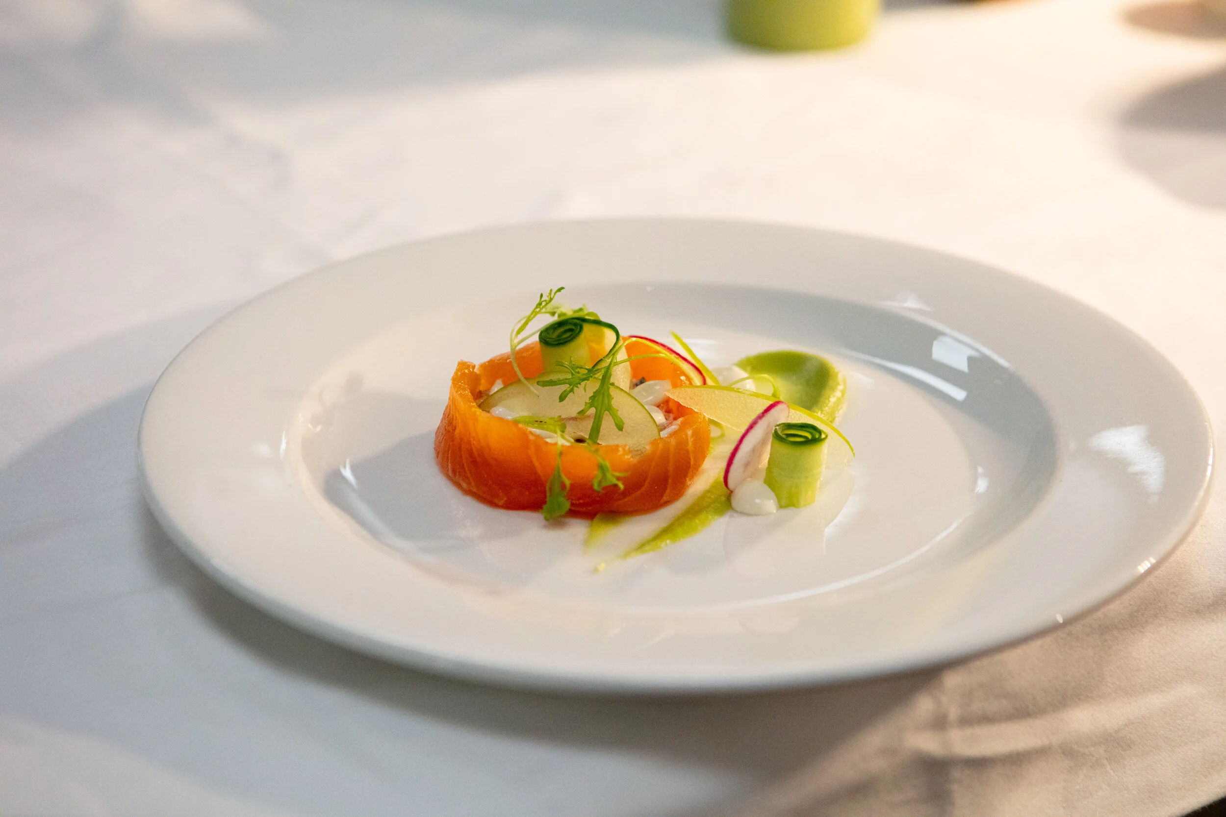 A gourmet dish with smoked salmon, thinly sliced radishes, microgreens, and a sauce on a white plate.