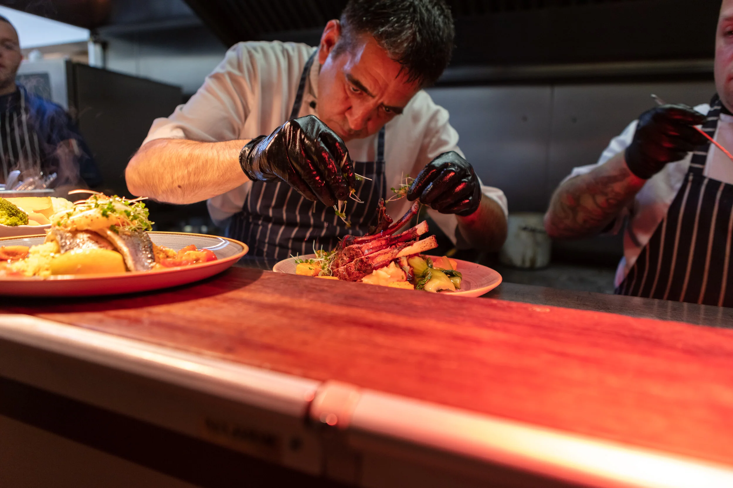A chef garnishing plated dishes in a restaurant kitchen with multiple plates of food on the counter.
