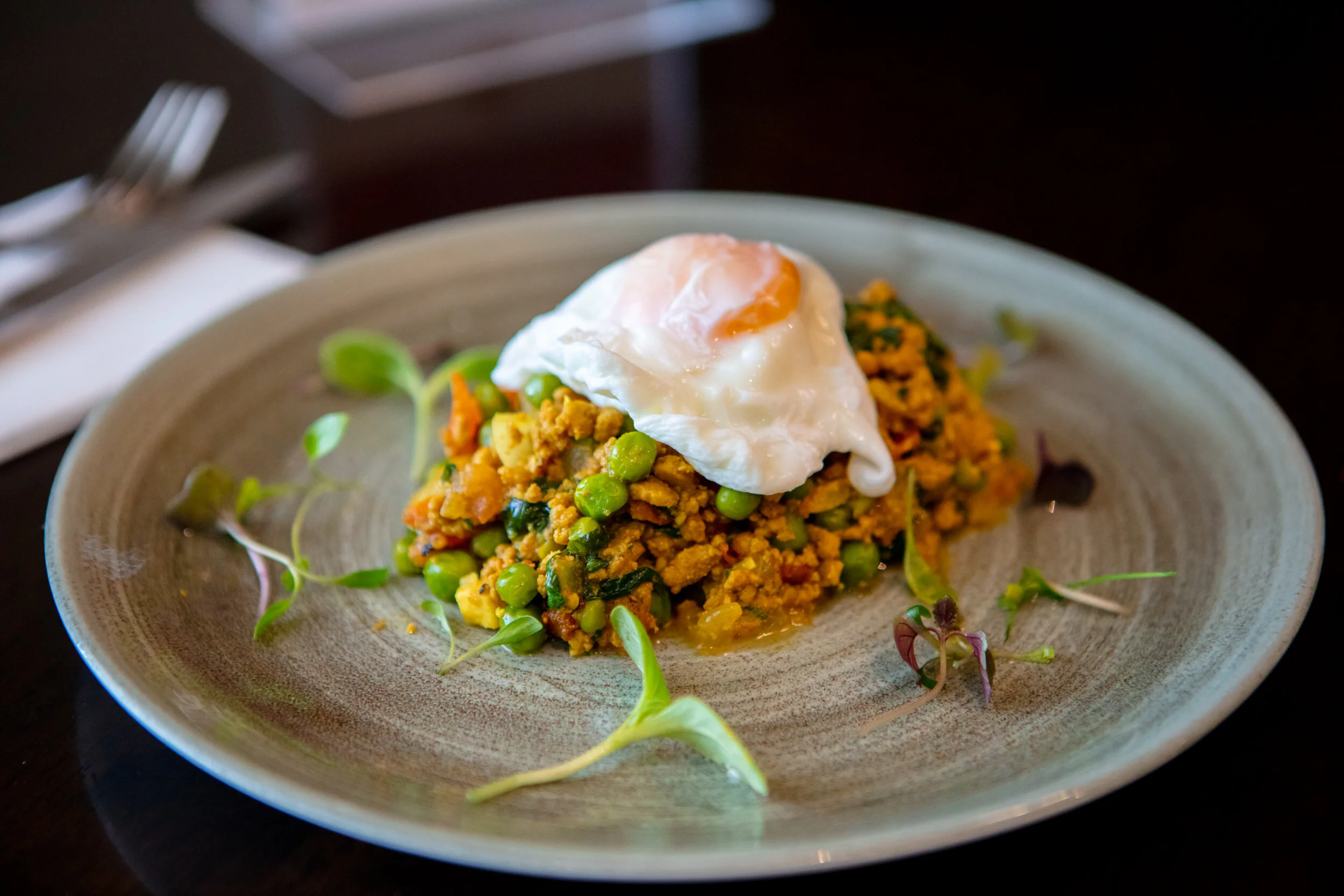 A plate of scrambled tofu with peas, topped with a poached egg, served on a ceramic plate garnished with microgreens.