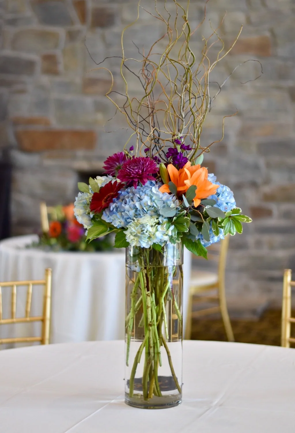 Tall centerpiece in glass cylinder with jewel toned flowers by Lark Floral 