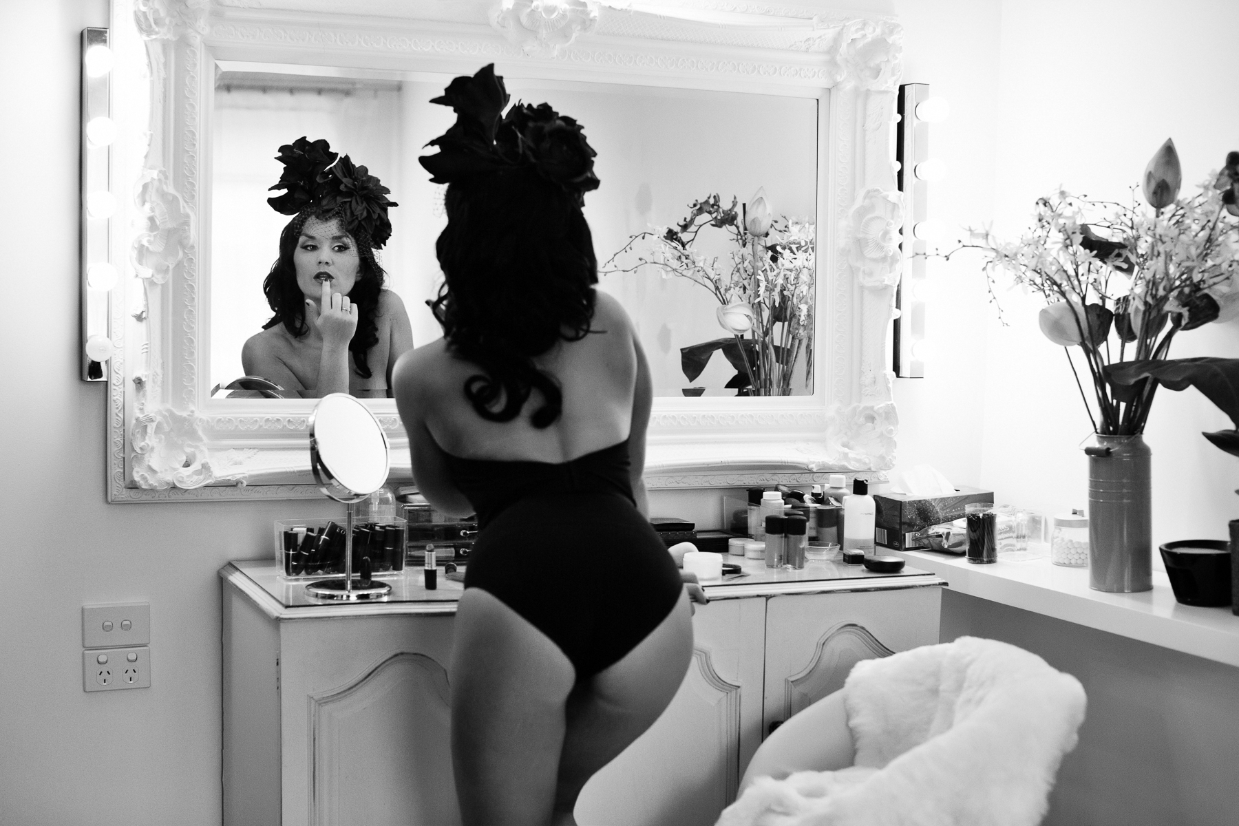 dark hair woman wearing a corset and flower headpiece leaning  to look in the mirror 