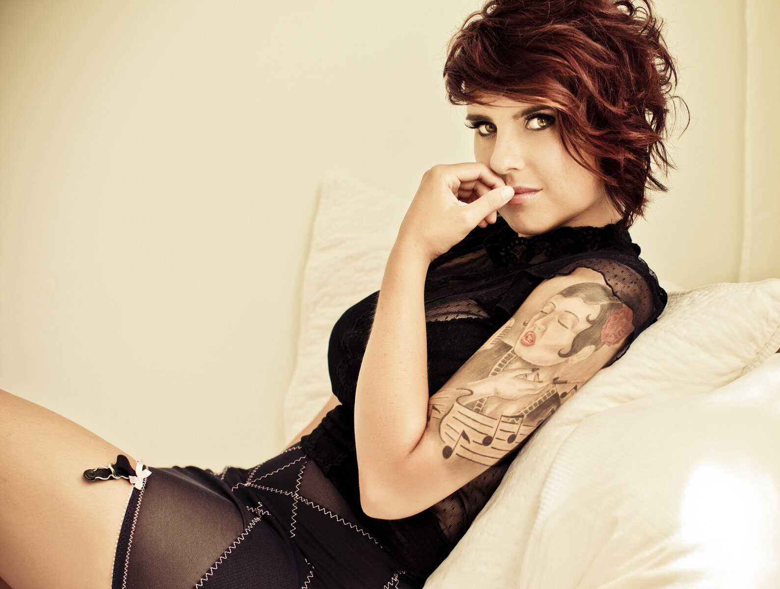 photo of dark short hair woman with sleeve tattoos sitting on a bed