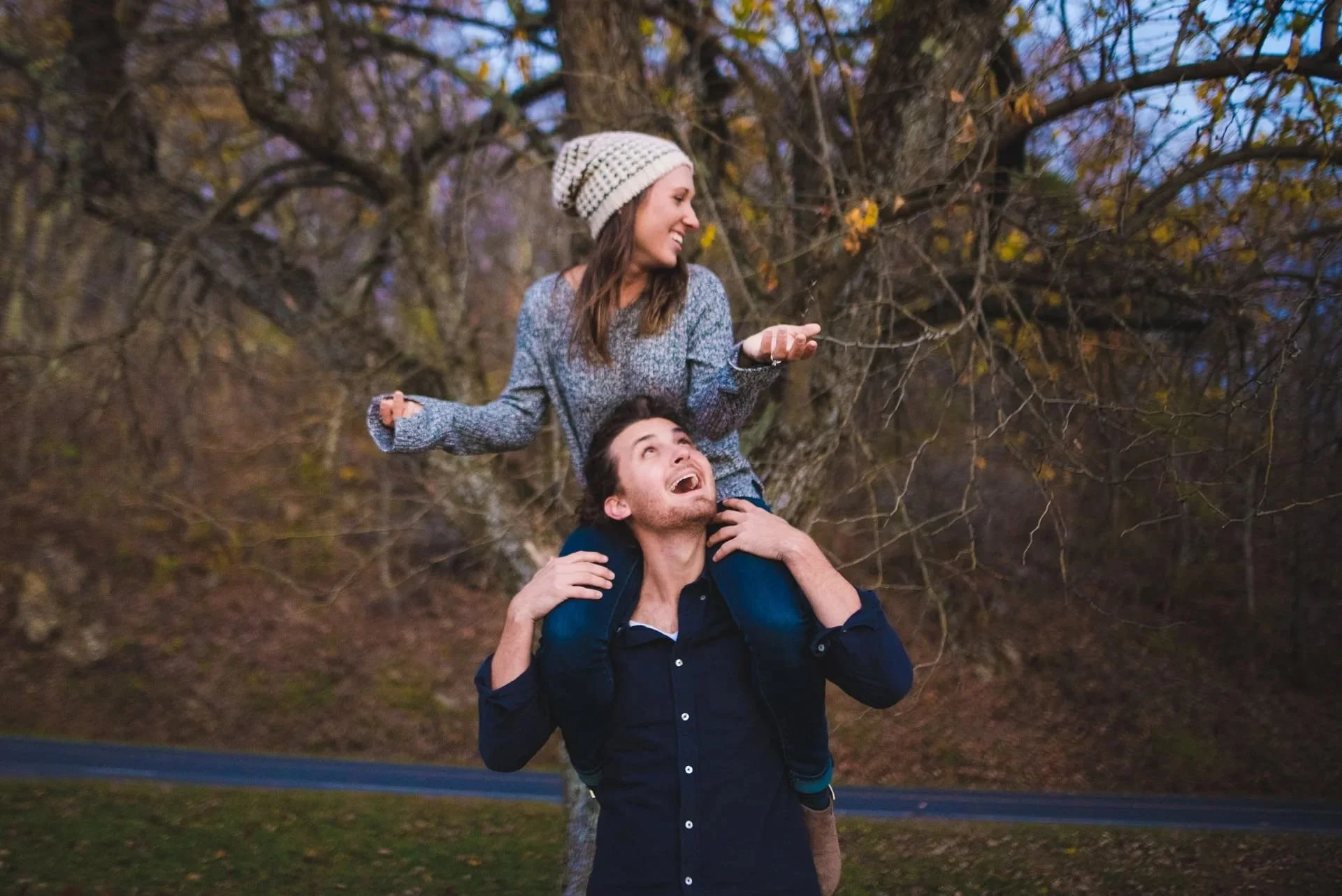 Playful engagement photo of a couple with piggyback pose on a forest trail in Shenandoah National Park during fall season.
