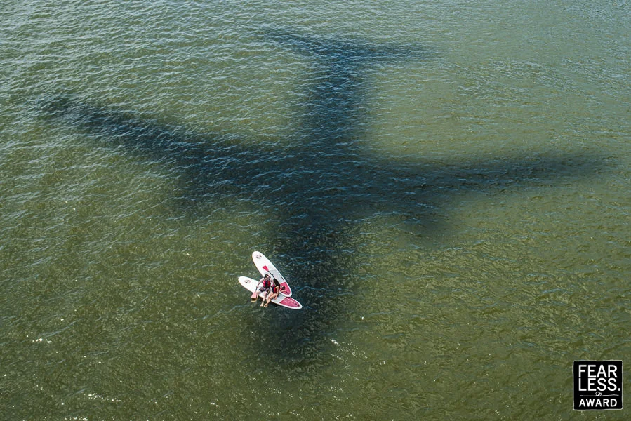 A couple on paddle boards beneath bridge shadows with a Fearless award mark