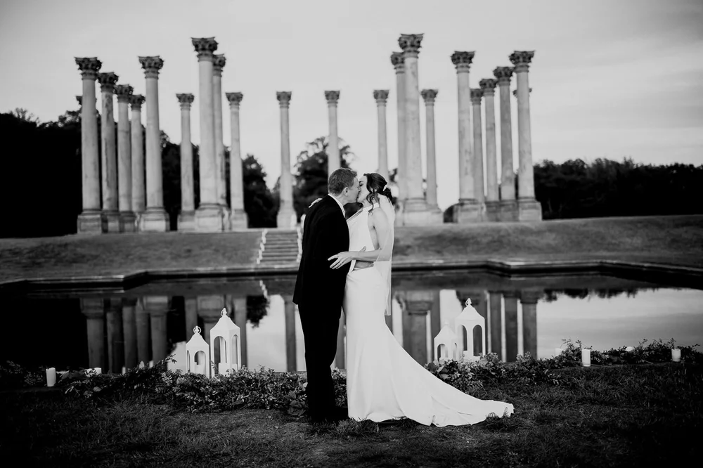 Black and white wedding portrait of bride and groom kissing by the reflecting pool at the Capitol Columns