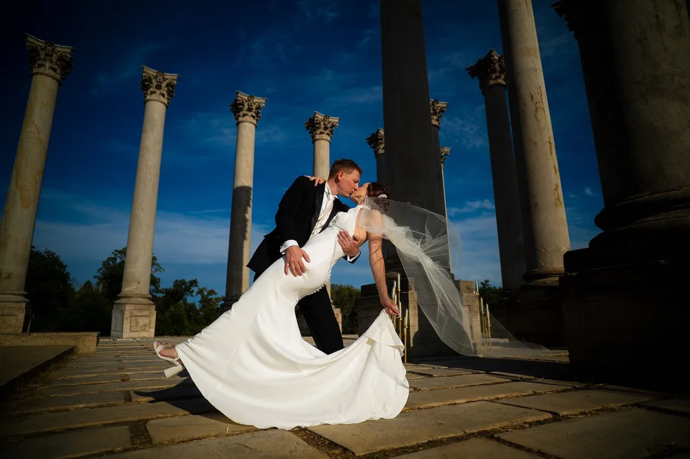 Bride and groom sharing a romantic dip kiss in front of the Capitol Columns at the National Arboretum