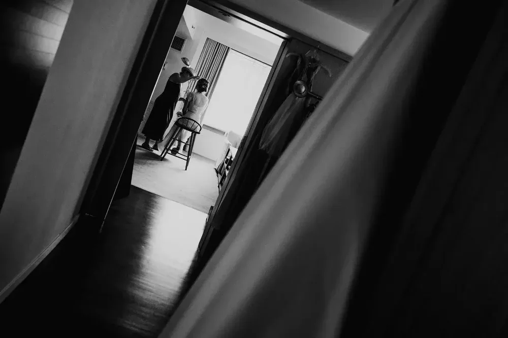 Black and white photo of bride getting ready, seen through a doorway with wedding dress in foreground at Meridian House