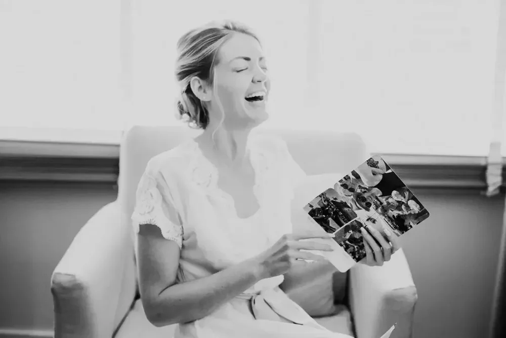 Bride laughing while looking at a photo book in a black and white getting ready moment at Meridian House