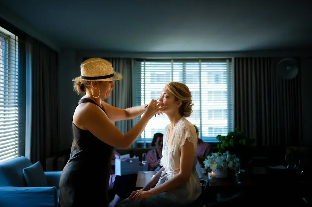 Makeup artist applying makeup to the bride as bridesmaids relax in the background at Meridian House