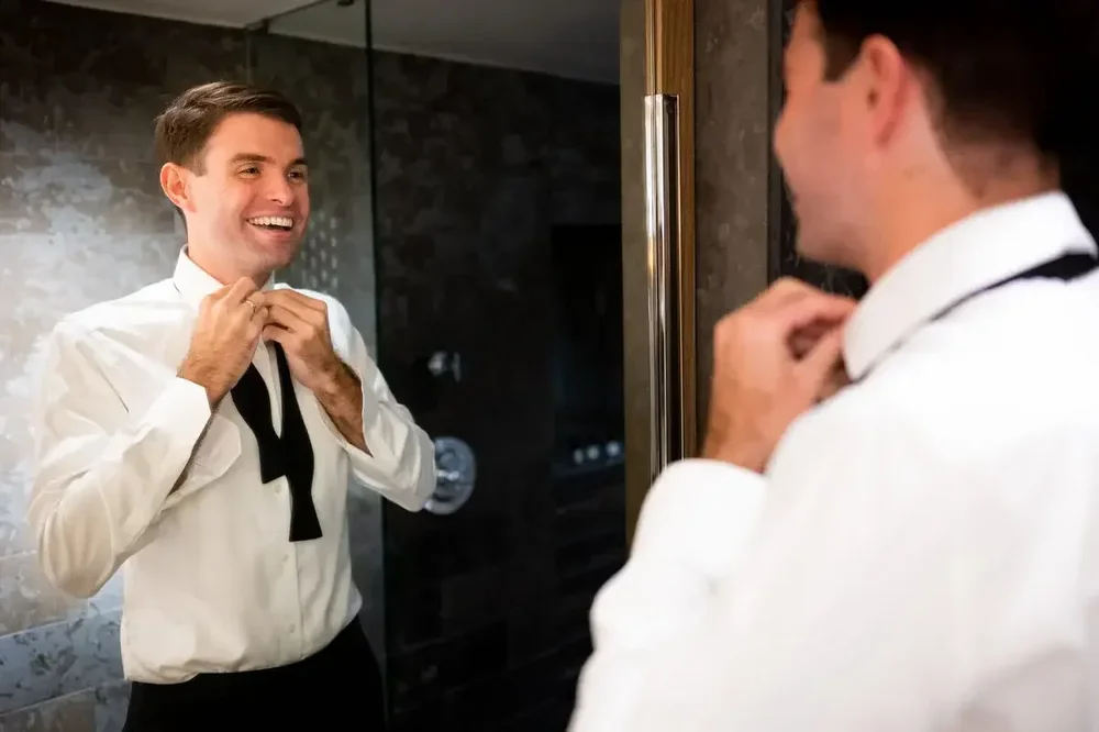 Groom smiling while adjusting his bow tie in the mirror before the Meridian House wedding ceremony