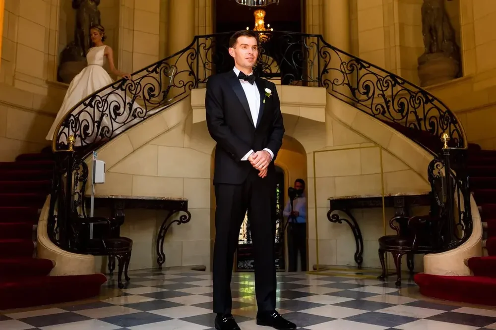Groom waits in the grand foyer as bride descends the iconic staircase at Meridian House