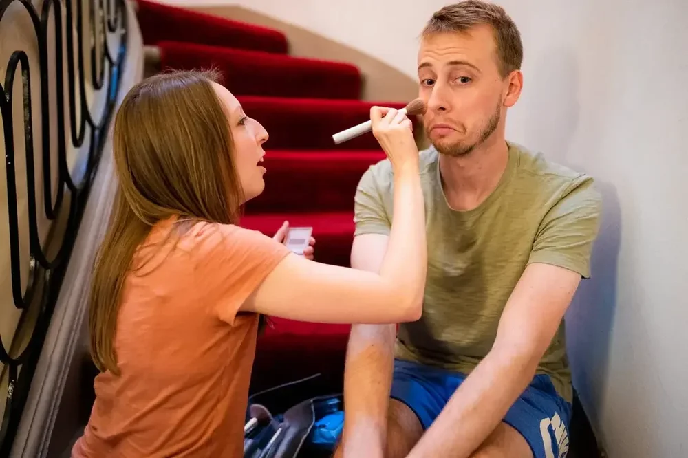 Groom getting makeup applied on the grand red staircase at Meridian House wedding in DC
