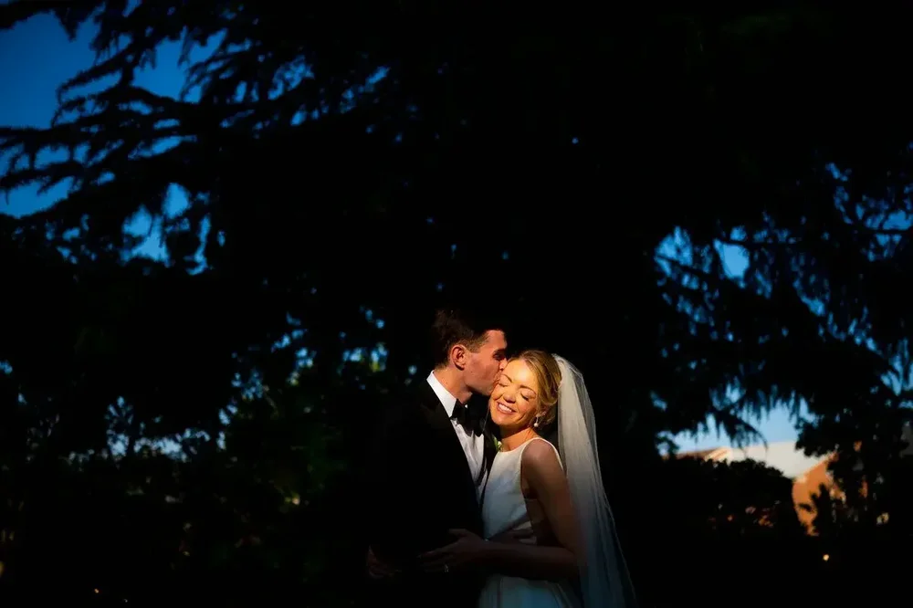 Romantic silhouette of groom kissing bride at sunset by the trees at Meridian House