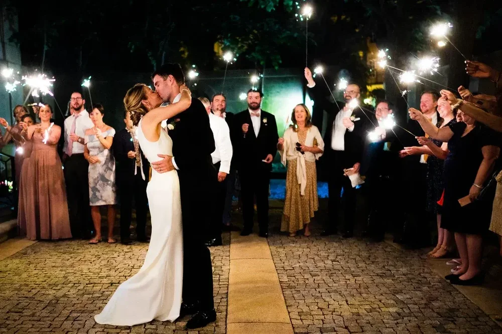 Bride and groom kissing during a sparkler exit surrounded by guests at Meridian House