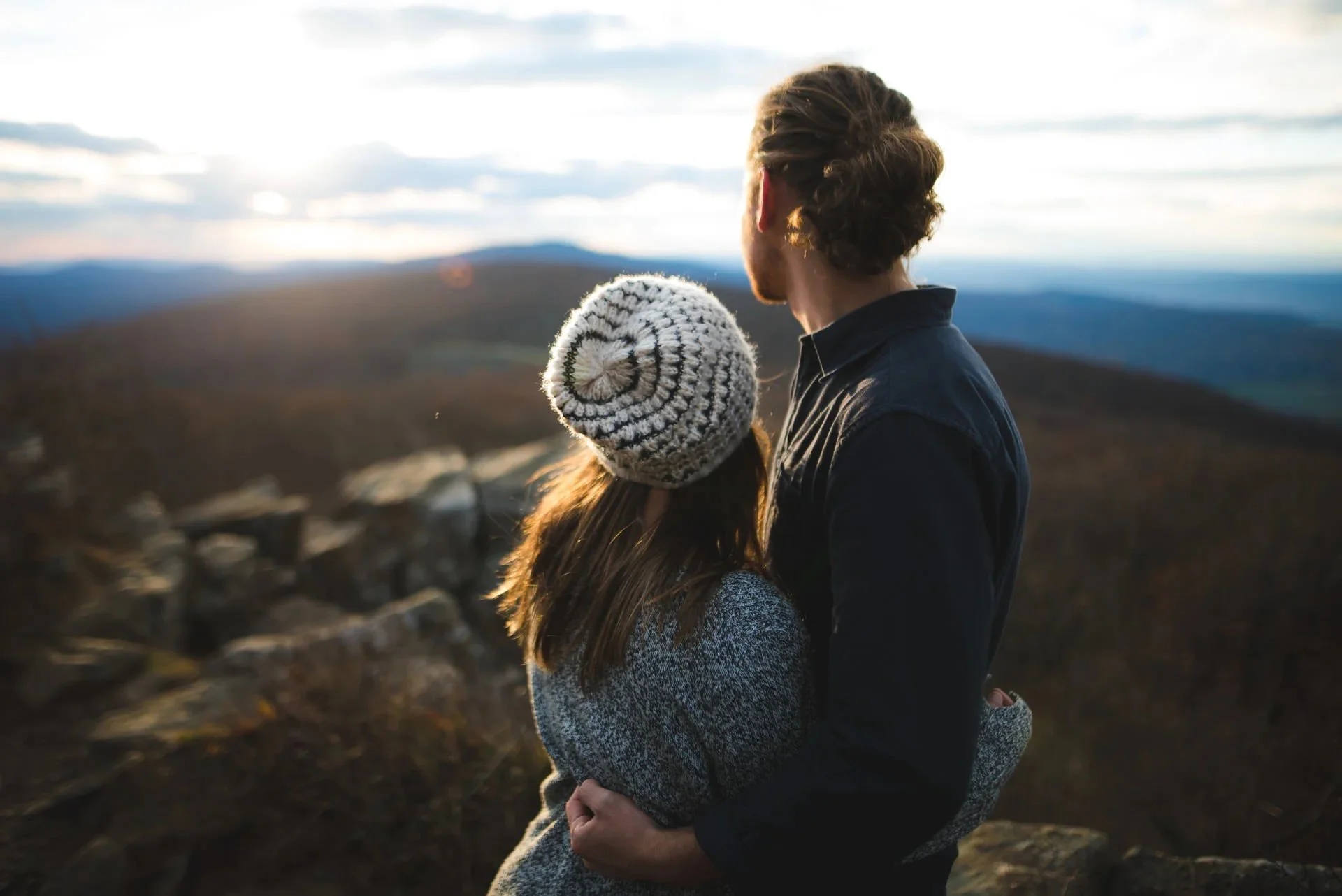 Couple embracing and looking at sunset over the Blue Ridge Mountains during a Shenandoah National Park engagement session at a scenic overlook.
