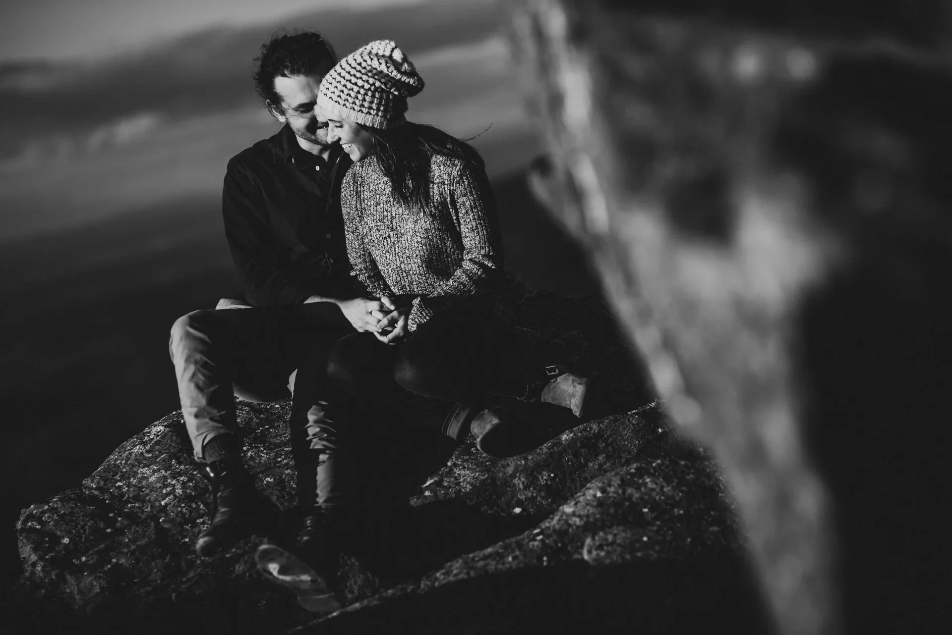 Couple sitting close together on rocky overlook during Shenandoah National Park engagement session in black and white, sharing a quiet intimate moment.