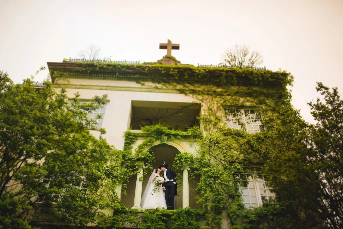 Wedding portrait near the Capitol in Washington DC with bride and groom kissing on a vine-covered balcony surrounded by lush greenery.