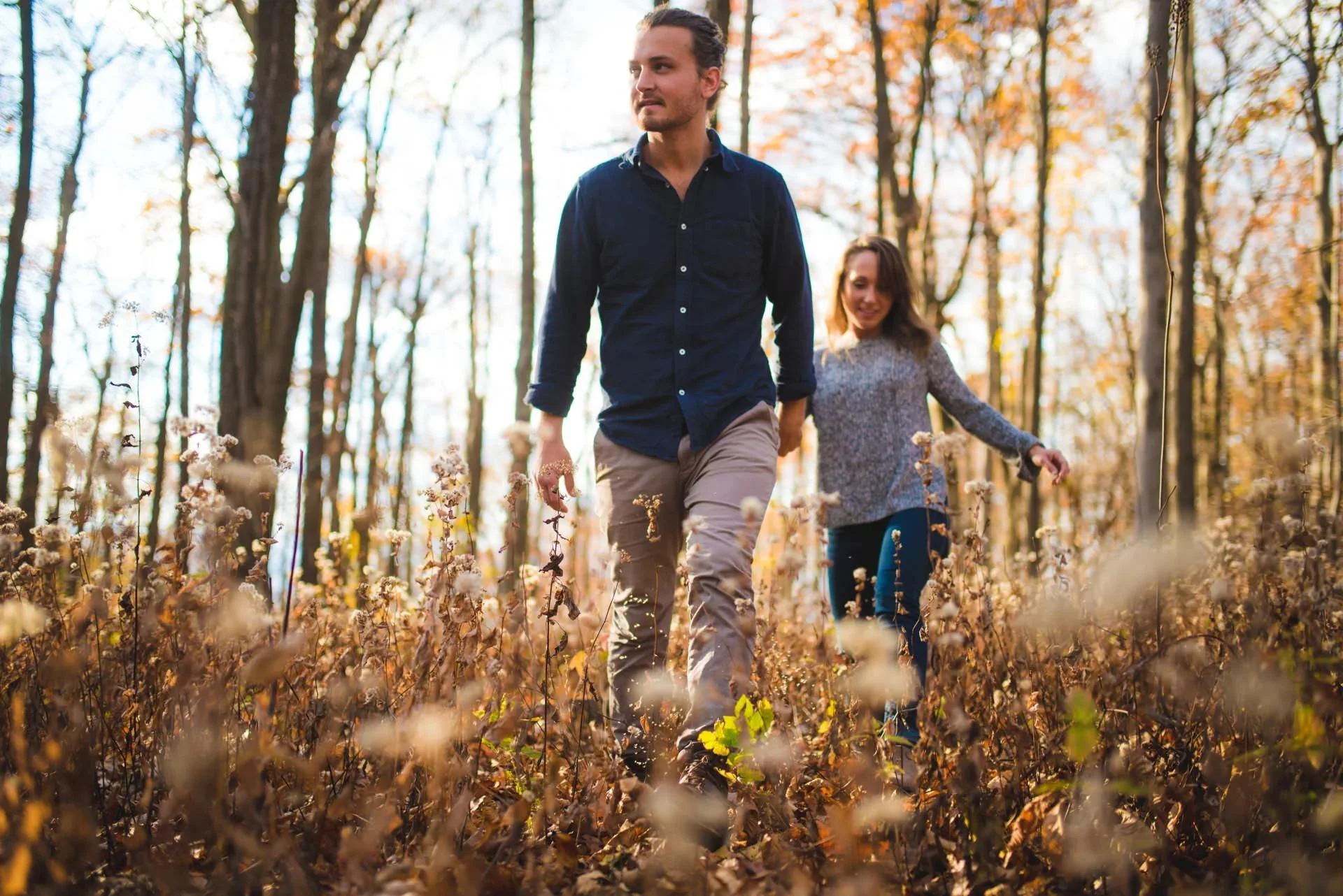Couple walking through forest during Shenandoah National Park engagement photos in warm fall light, natural candid moment outdoors.