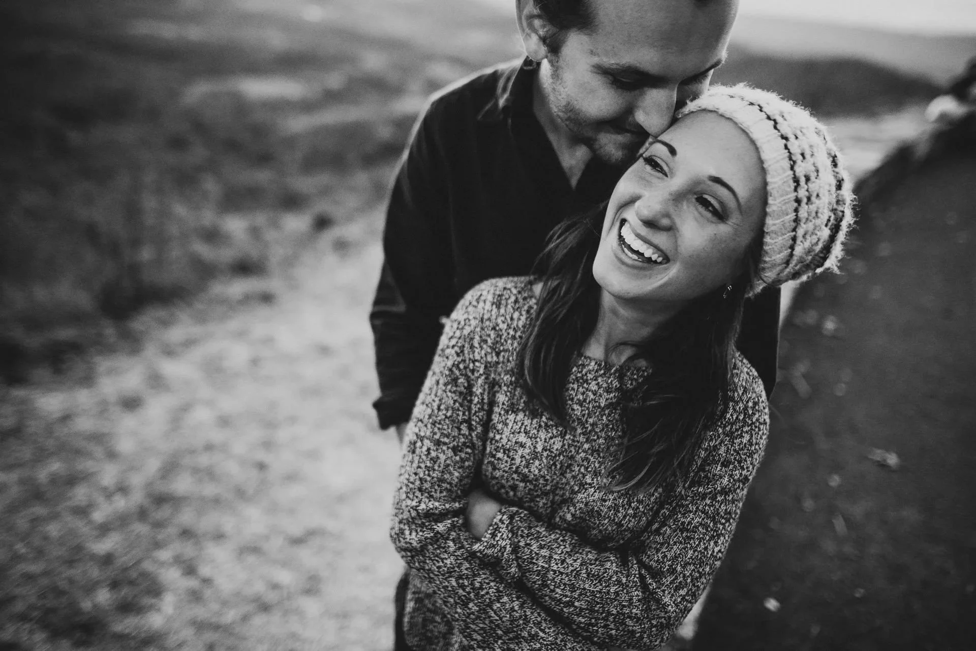 Black and white candid engagement photo of a laughing couple on a trail in Shenandoah National Park with intimate close-up composition.