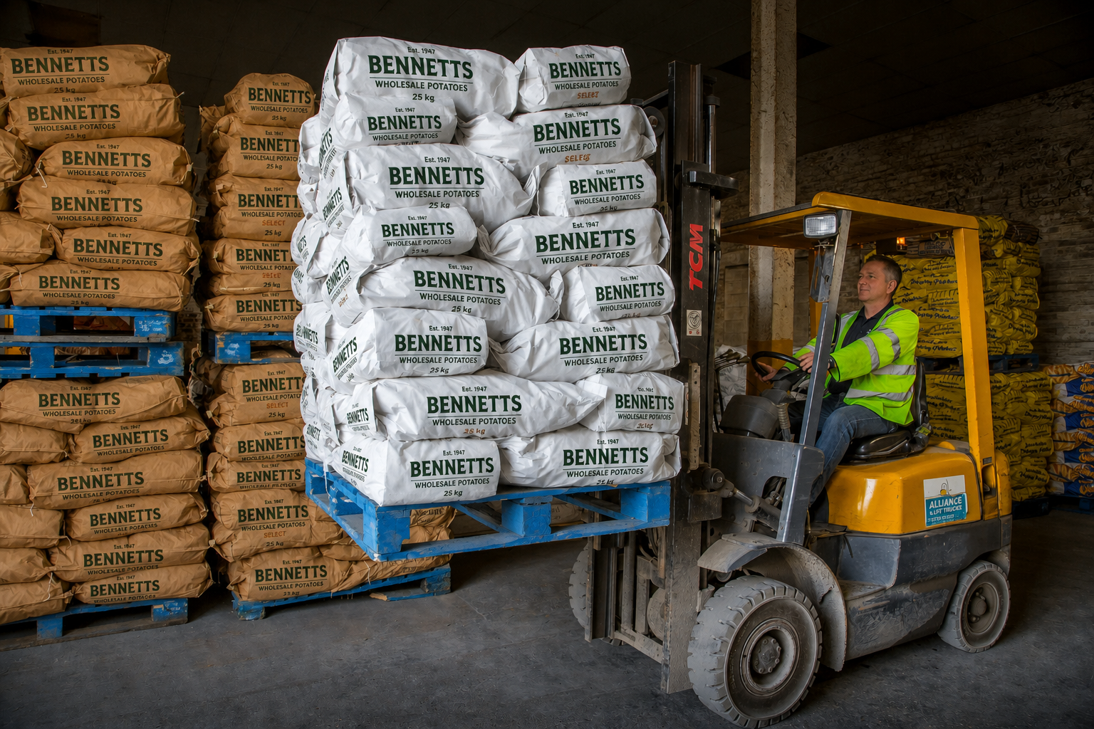 Person in a high-visibility jacket operating a forklift inside a warehouse, moving bags of wholesale potatoes labeled 'Bennetts' stacked on pallets.