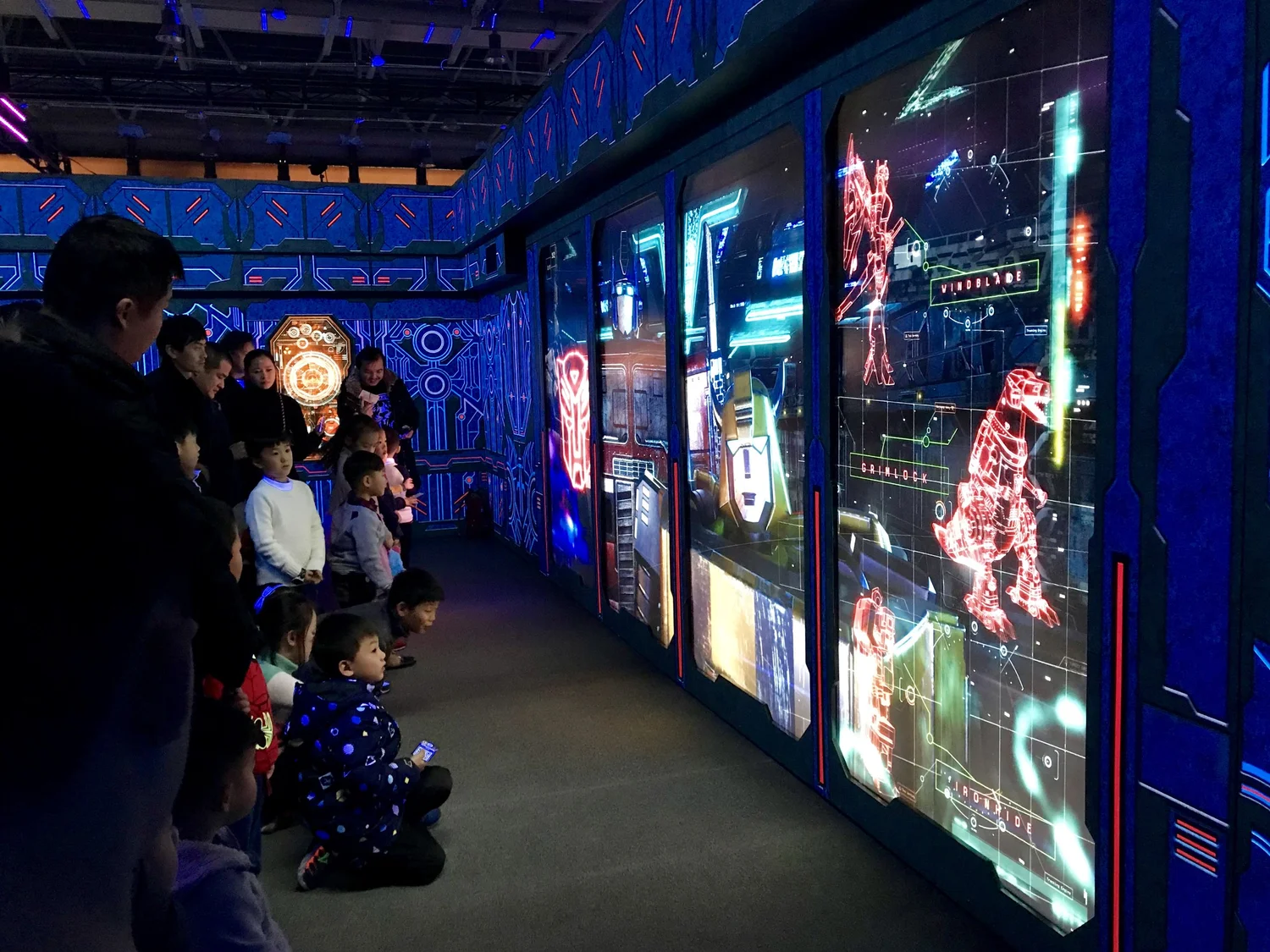 Children and adults watching a large interactive digital screen with futuristic sci-fi graphics in a themed exhibit.