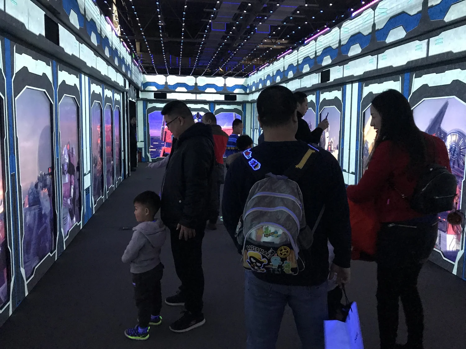 Group of people, including children, inside a colorful, illuminated hallway with artwork of Star Wars characters on the walls.