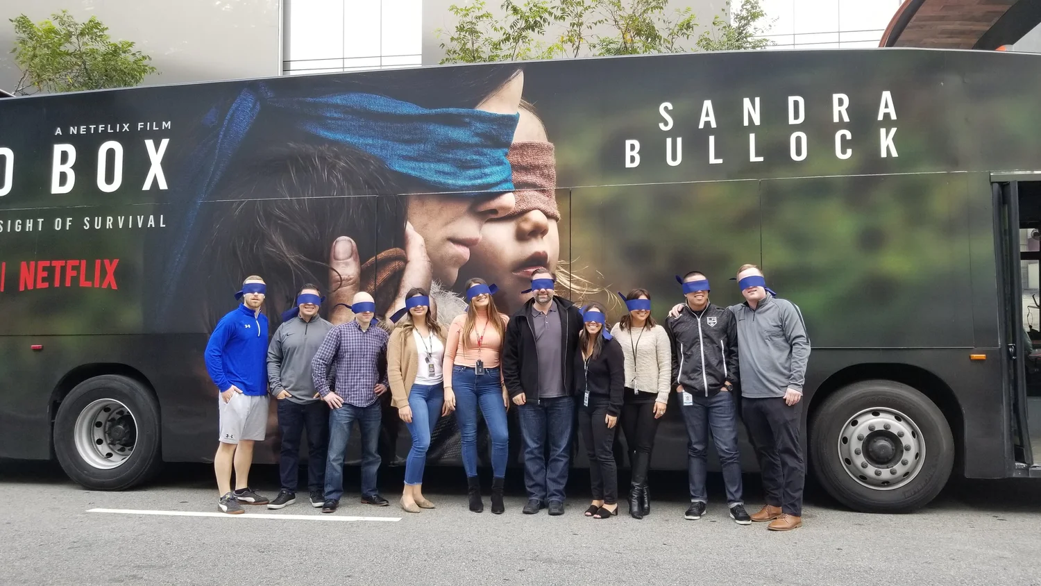Group of nine people standing in front of a Netflix film bus promoting 'Blind Box' with a large poster of two children blindfolded.