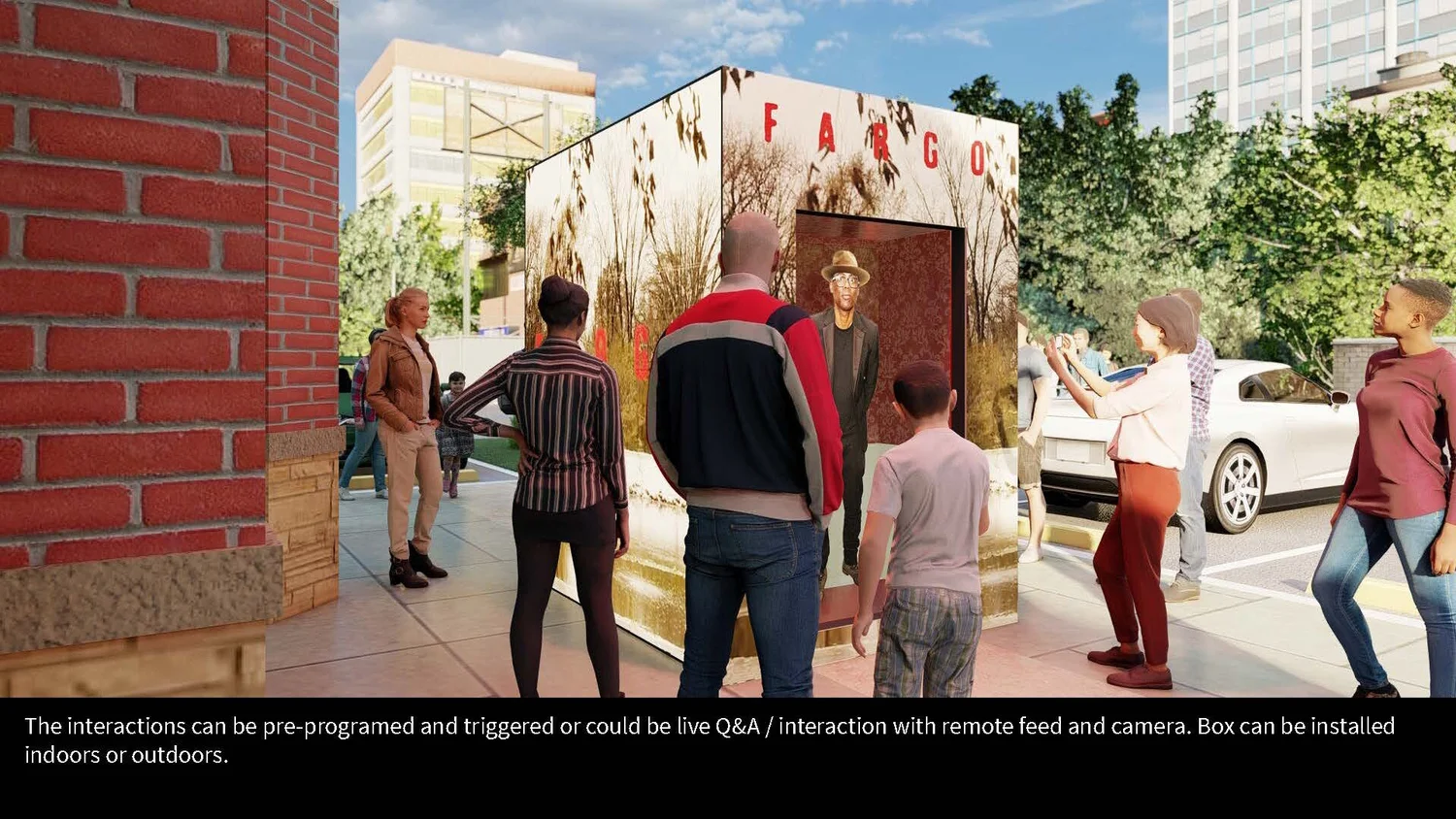 People gathered outdoors around an interactive display box with the word Fargo on top. The display shows a man in a hat. The setting appears to be a city sidewalk with cars and green trees in the background.