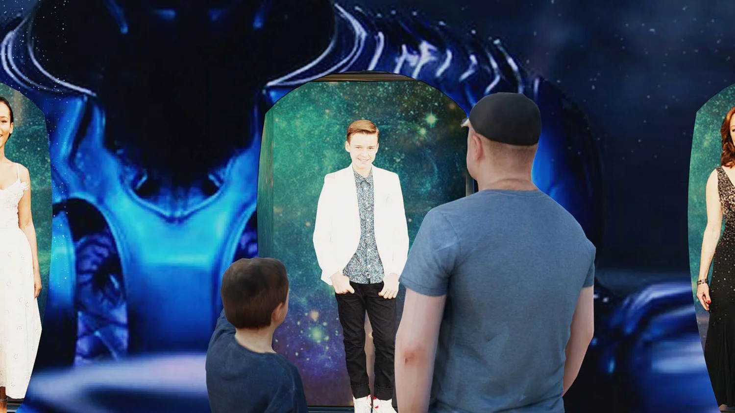 A boy and a man are looking at a holographic display of a smiling young woman dressed in a white jacket and dark pants. The background showcases a space-themed display with stars and swirling blue patterns.