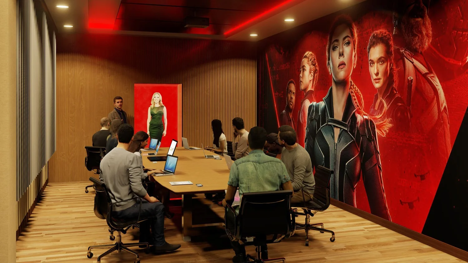 A group of people in a conference room with laptops, listening to a man standing at the front, with large 'Black Widow' movie poster on the wall.