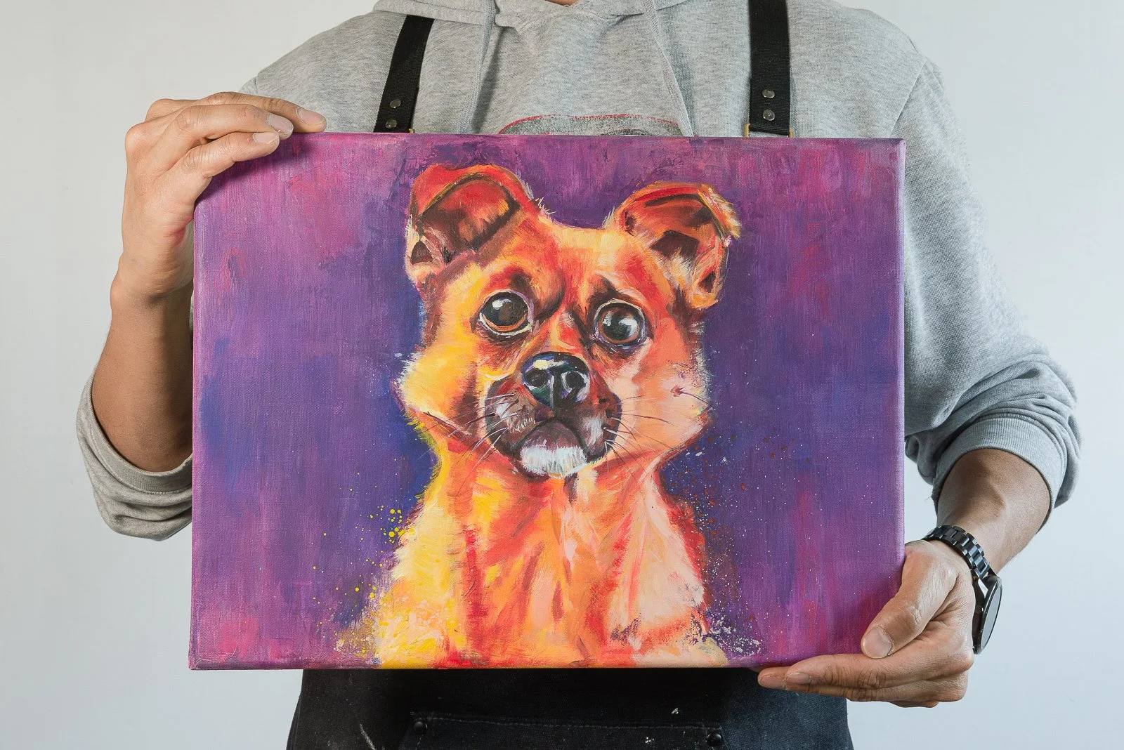 Person holding a colorful painting of a dog's face against a purple background.