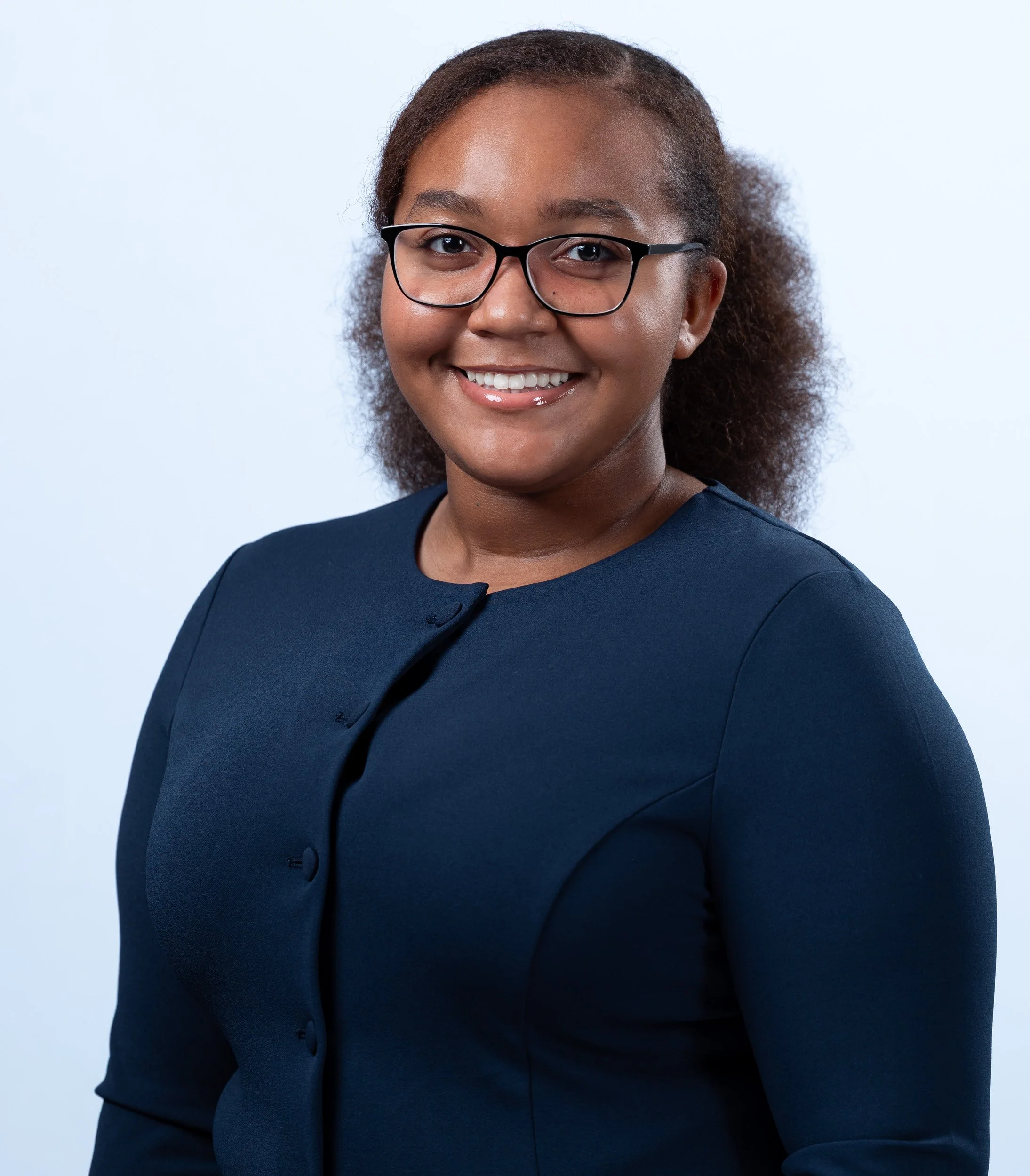 Corporate headshot of a professional woman wearing glasses and navy attire on a light gray background, created by a Maryland headshot photographer specializing in business portraits in the DC metro area.