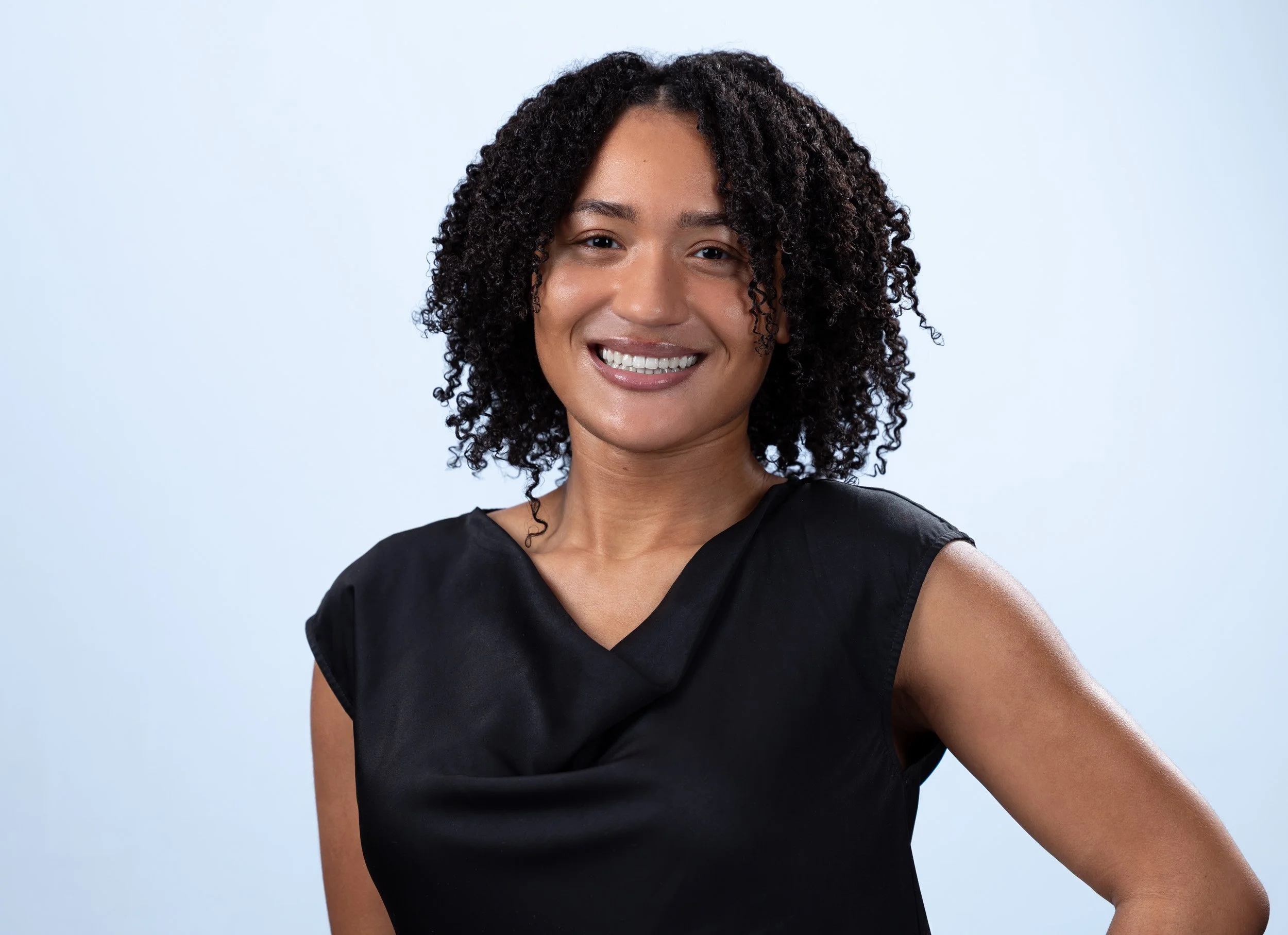 Modern professional headshot of a smiling woman in a black top with natural curly hair on a soft gray background, captured by a Maryland headshot photographer serving the Washington DC region.