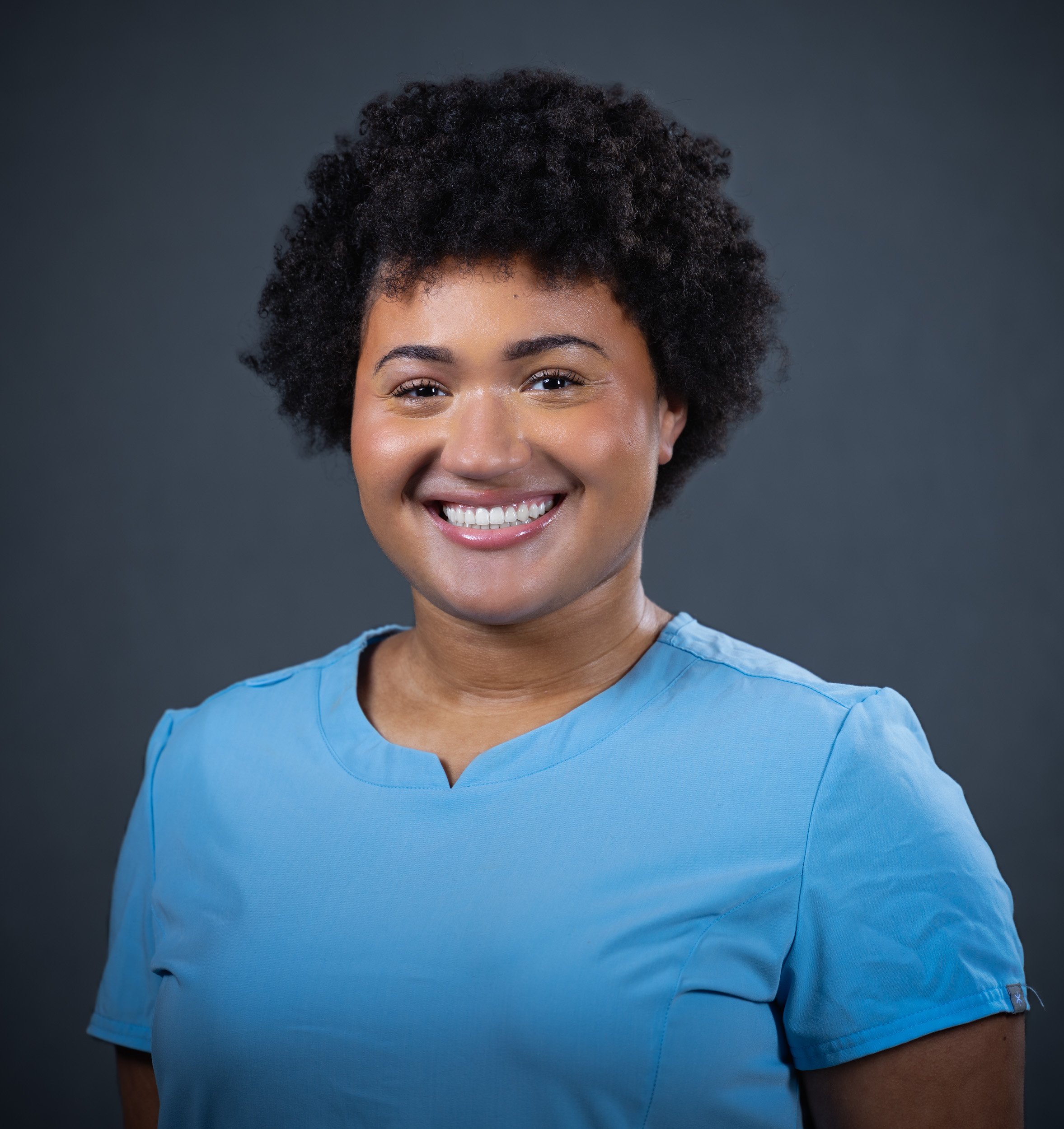 Professional healthcare headshot of a smiling female medical professional in blue scrubs on a clean studio background, photographed by a Maryland headshot photographer serving Washington DC and Northern Virginia.