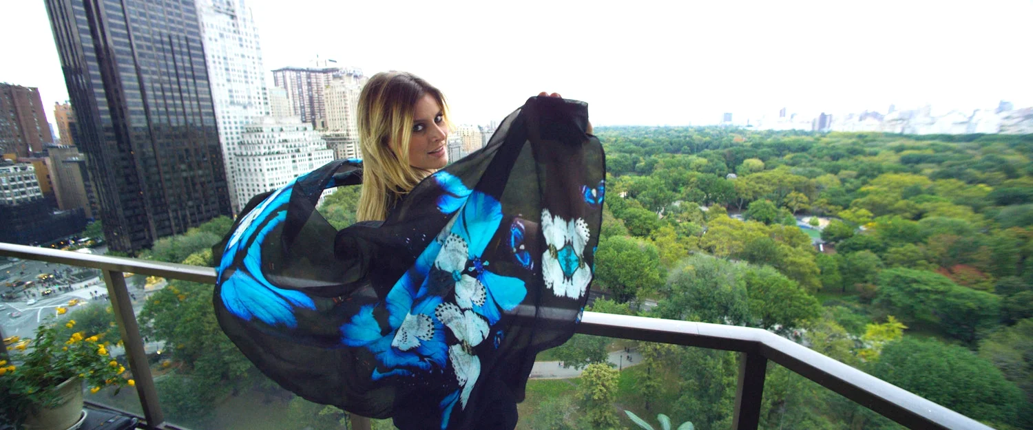 Woman standing on a balcony overlooking New York City with a large black and blue shawl.