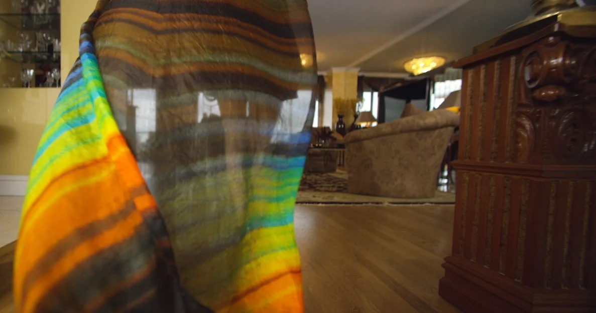 Close-up of a colorful rainbow tie-dye cloth draped over a piece of outdoor furniture in a living room.