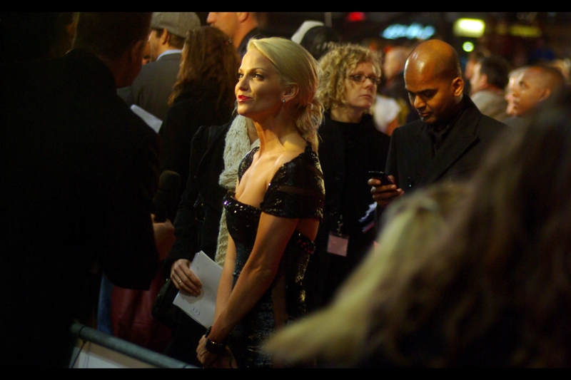 Singer / Actress Sarah Harding does NOT laugh, presumably as the reporter's line of question goes something like : ”Sarah, welcome to the premiere : love the dress. But what our viewers really want to know is what IS the guy behind you texting, and who is he texting it to??”