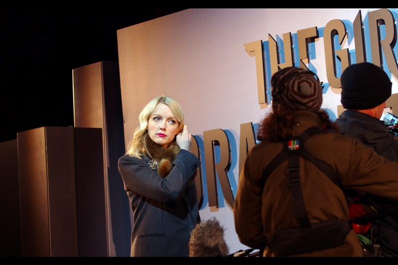 Your host for this evening will be blonde, glamorous, and adjusting her hair/head-set for a little while to make sure the angle it sits at won't mortally offend Daniel Craig.