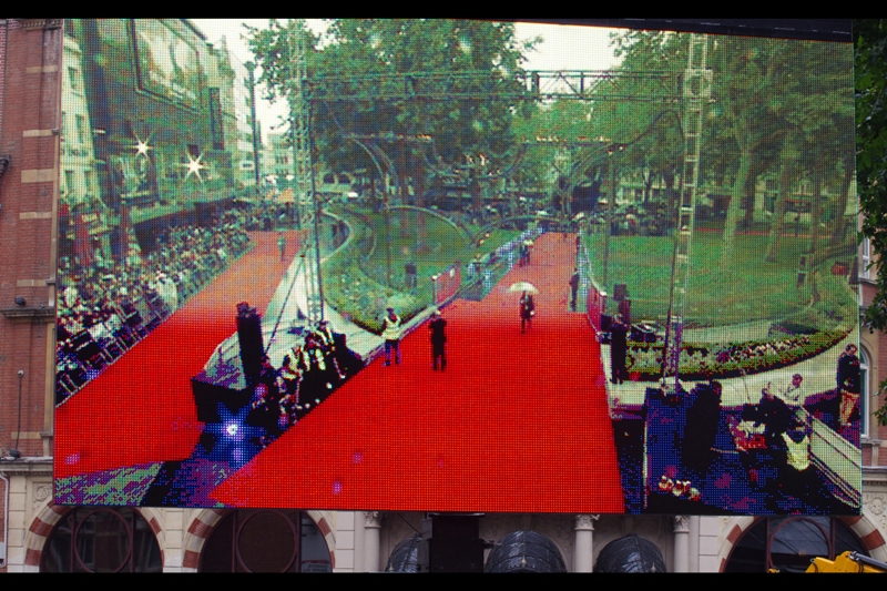 View from a TV Screen across from me. Two prongs of the three-pronged red carpet (my spot was near the corner on the left, with a long view of the Batman cowl and stage). The forecast was for rain, autograph dealers and Marion Cotillard. And all three eventuated!