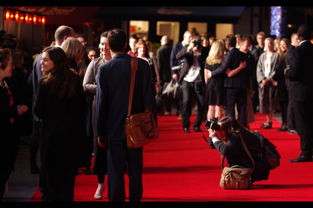 The crowd continues to mill at every possible angle on the carpet, while entourages, attendants, scribes and secretaries hold satchels, .... and even the people on the red carpet (who should be asked to move on into the cinema) are having to get inventive with the unsanctioned photography.